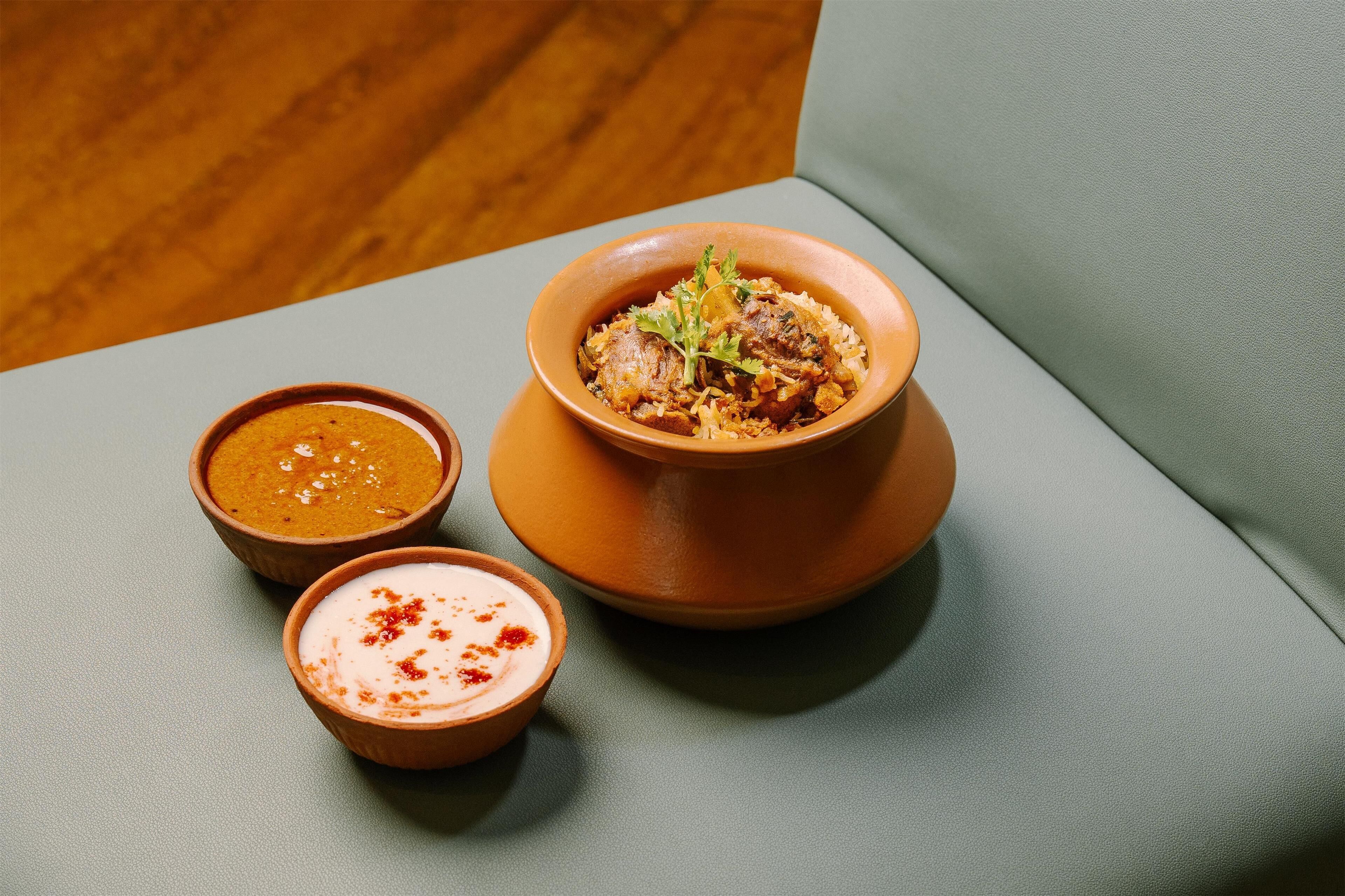 Una mesa con un tazón de arroz y carne, dos tazones pequeños de salsa, y una silla tapizada de verde.