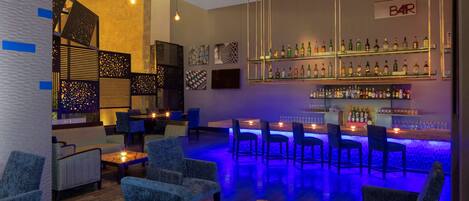 Zona de bar con diversas opciones de asiento, barra bien surtida y decoración en las paredes.