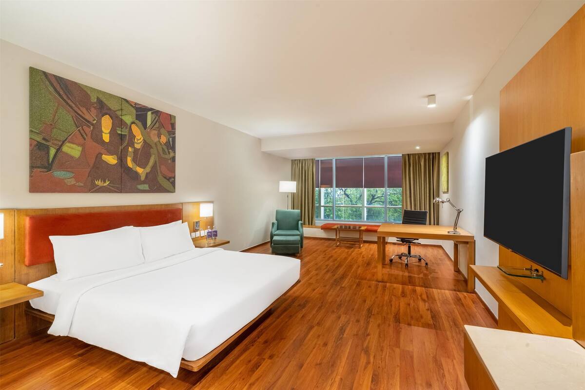 Ein Hotelzimmer mit einem großen Bett, einem Schreibtisch, einem Sessel, einem Fernseher und einem Bild an der Wand.