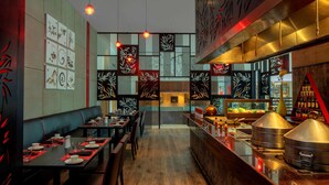 A restaurant with a long counter, tables, and chairs. There are decorative panels on the walls and a counter with food items. - Radisson Blu Plaza Hotel Hyderabad Banjara Hills (Hyderabad)