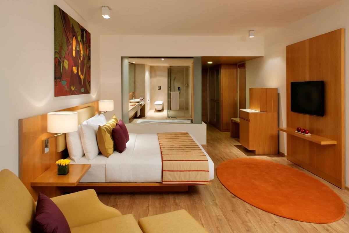 Ein modernes Hotelzimmer mit Bett, Nachttisch, Fernseher und einem durch eine geöffnete Tür einsehbaren Badezimmer.