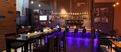 A bar area with a long counter, multiple stools, and a bar sign.