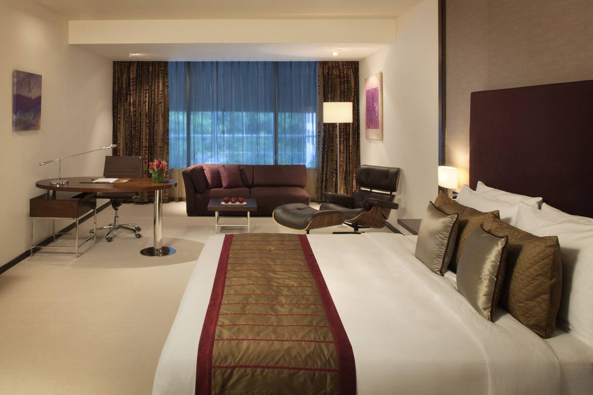 Ein Hotelzimmer mit einem großen Bett, einem Schreibtisch mit Stuhl, einer Couch und einem Fernseher.