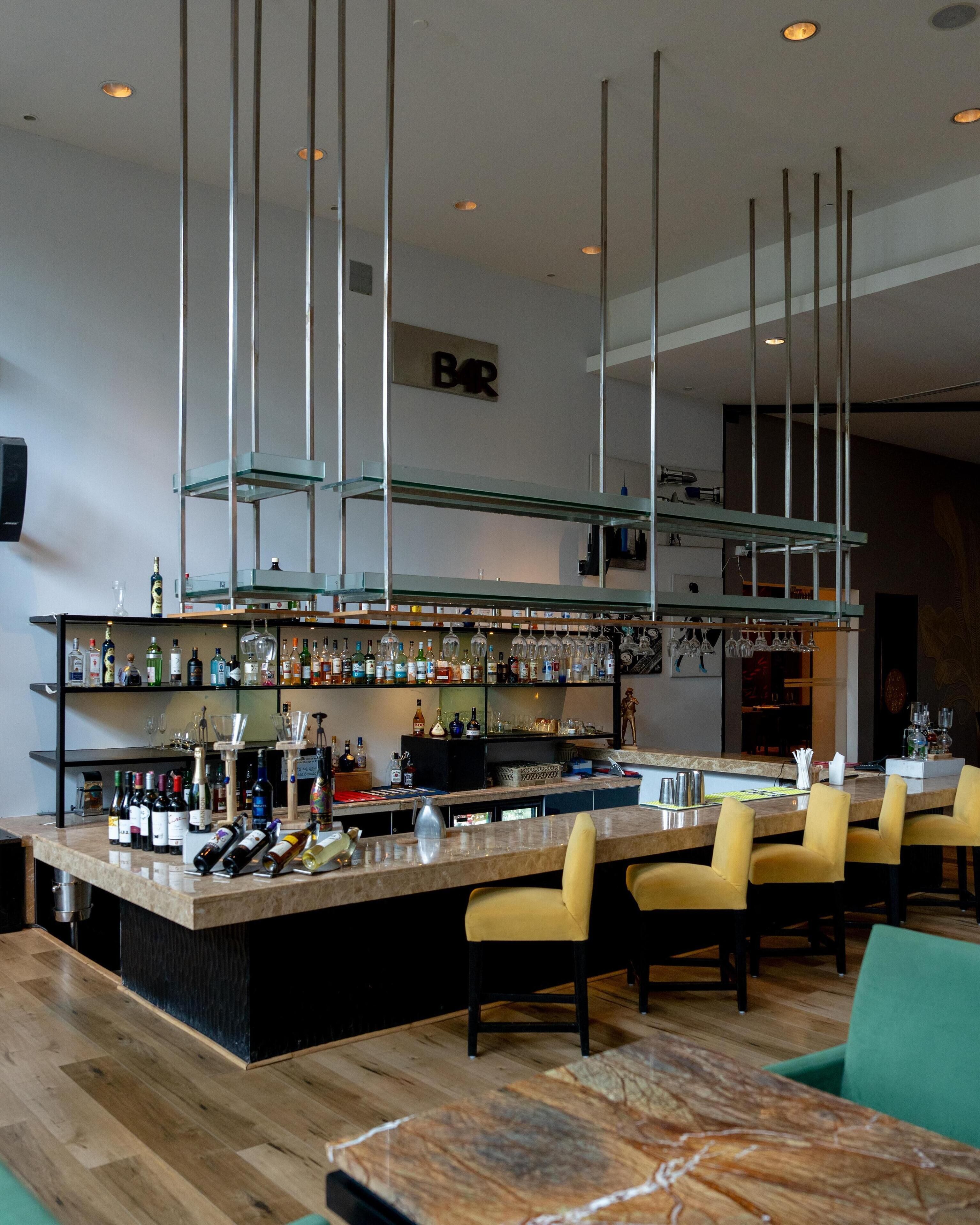 A bar area with a marble countertop, multiple shelves with bottles, glasses, and a 'BAR' sign on the wall.