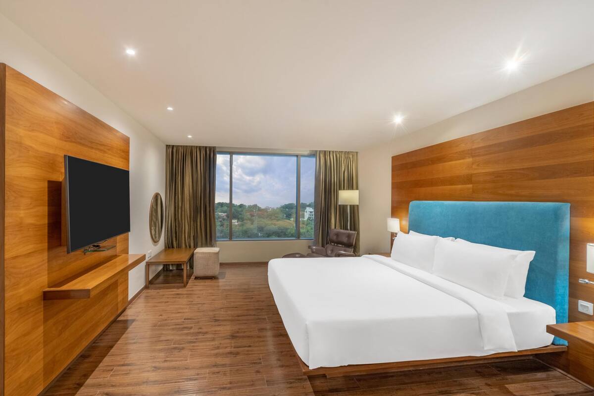 Ein Hotelzimmer mit einem großen Bett, einem Flachbildfernseher, einem Schreibtisch und Blick ins Freie.
