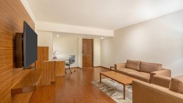 Una sala de estar moderna con un televisor de pantalla plana, piso de madera, un conjunto de sofás y un escritorio con una silla.