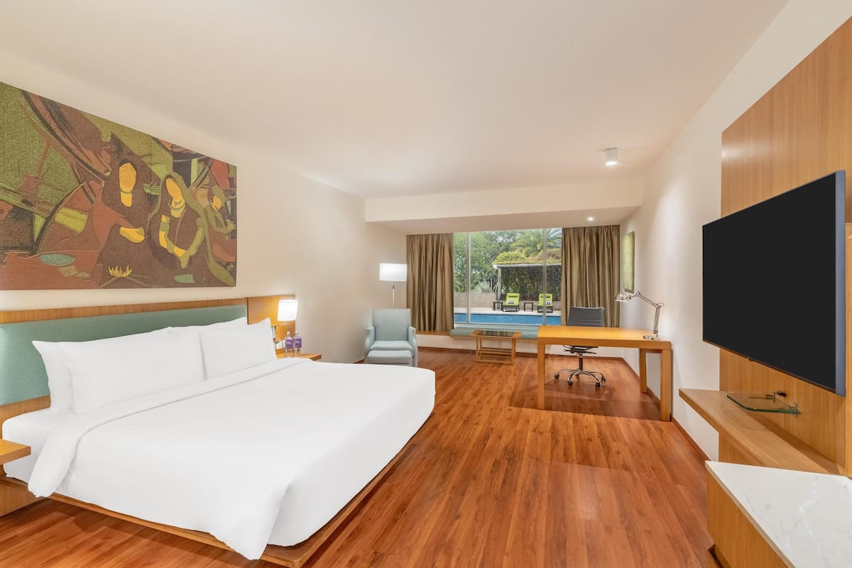 Ein Hotelzimmer mit einem großen Bett, einem Schreibtisch, einem Fernseher und Blick auf einen Poolbereich.