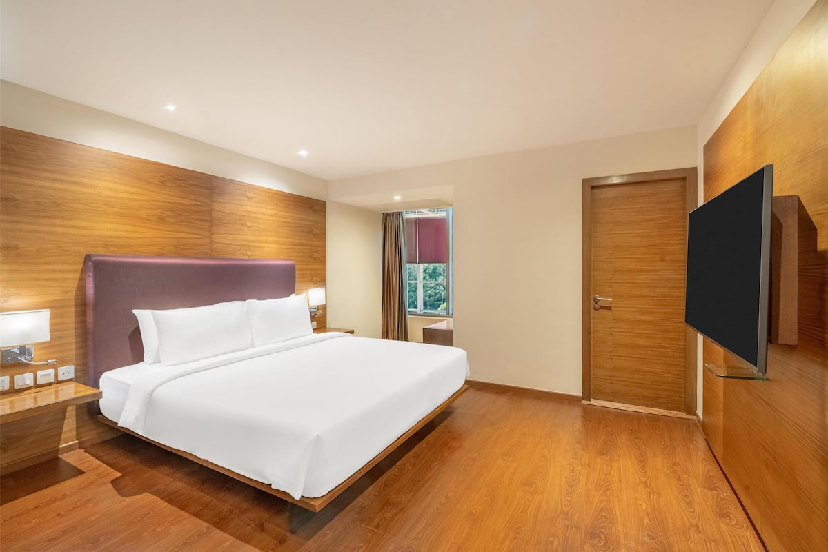 Ein modernes Hotelzimmer mit einem großen Bett, Holzvertäfelung an den Wänden, einem Flachbildfernseher und einem fenster mit Vorhängen.