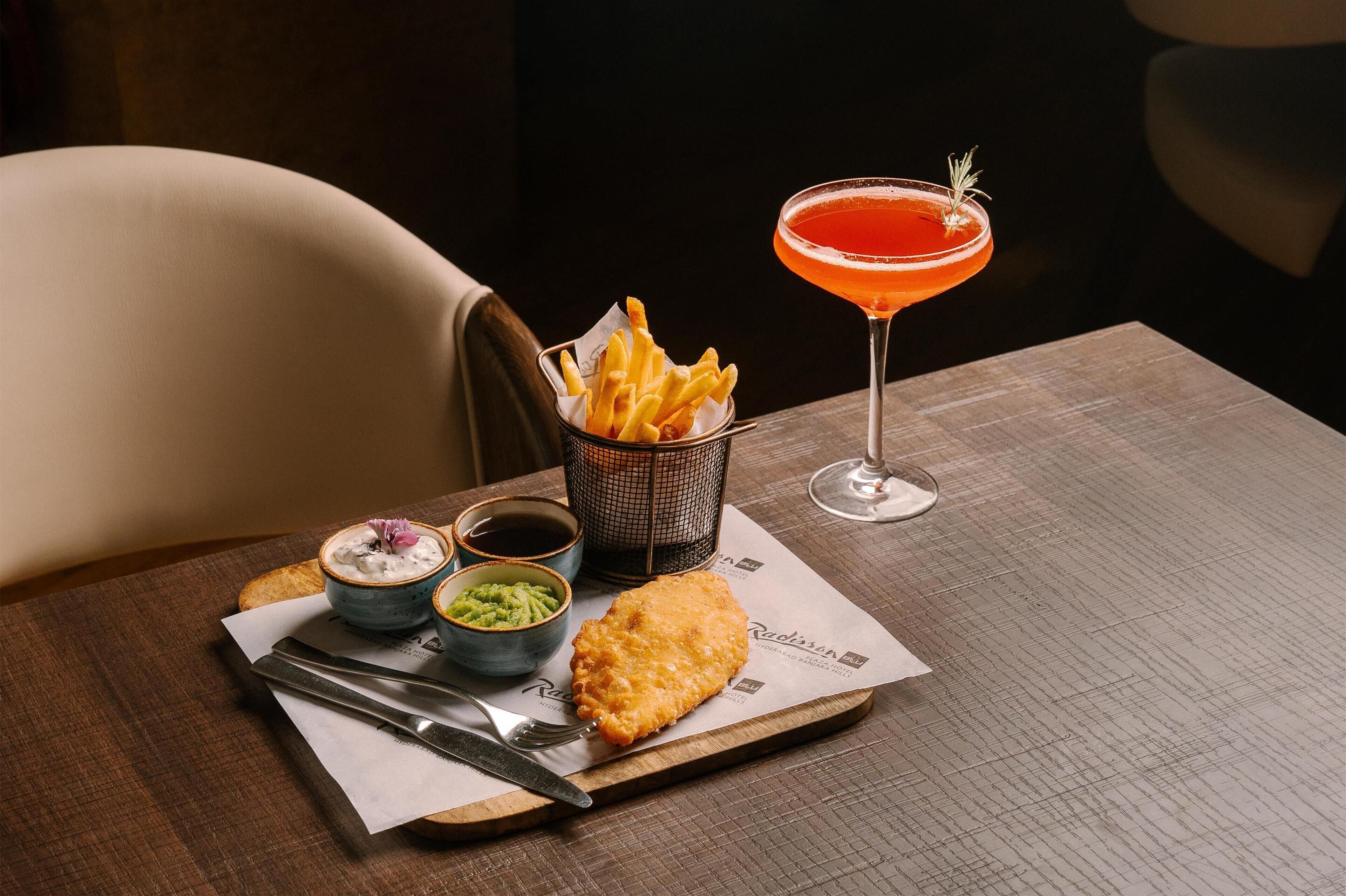 A meal tray with a breaded fish fillet, French fries, and two small bowls of dips on a wooden table.