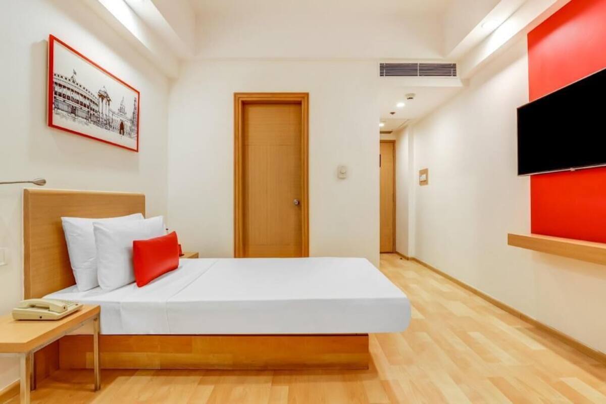 Ein Hotelzimmer mit Bett, Nachttisch, Wand-Fernseher und Tür.