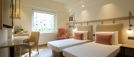 A hotel room with two beds, a desk, a chair, a window with a view, and a ceiling fan.
