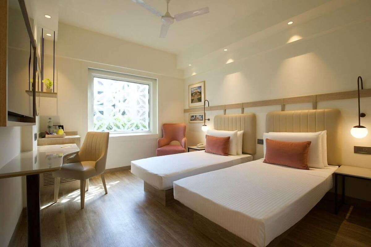 Ein Hotelzimmer mit zwei Betten, einem Schreibtisch, einem Sessel, einem Fenster mit Blick und einem Deckenventilator.