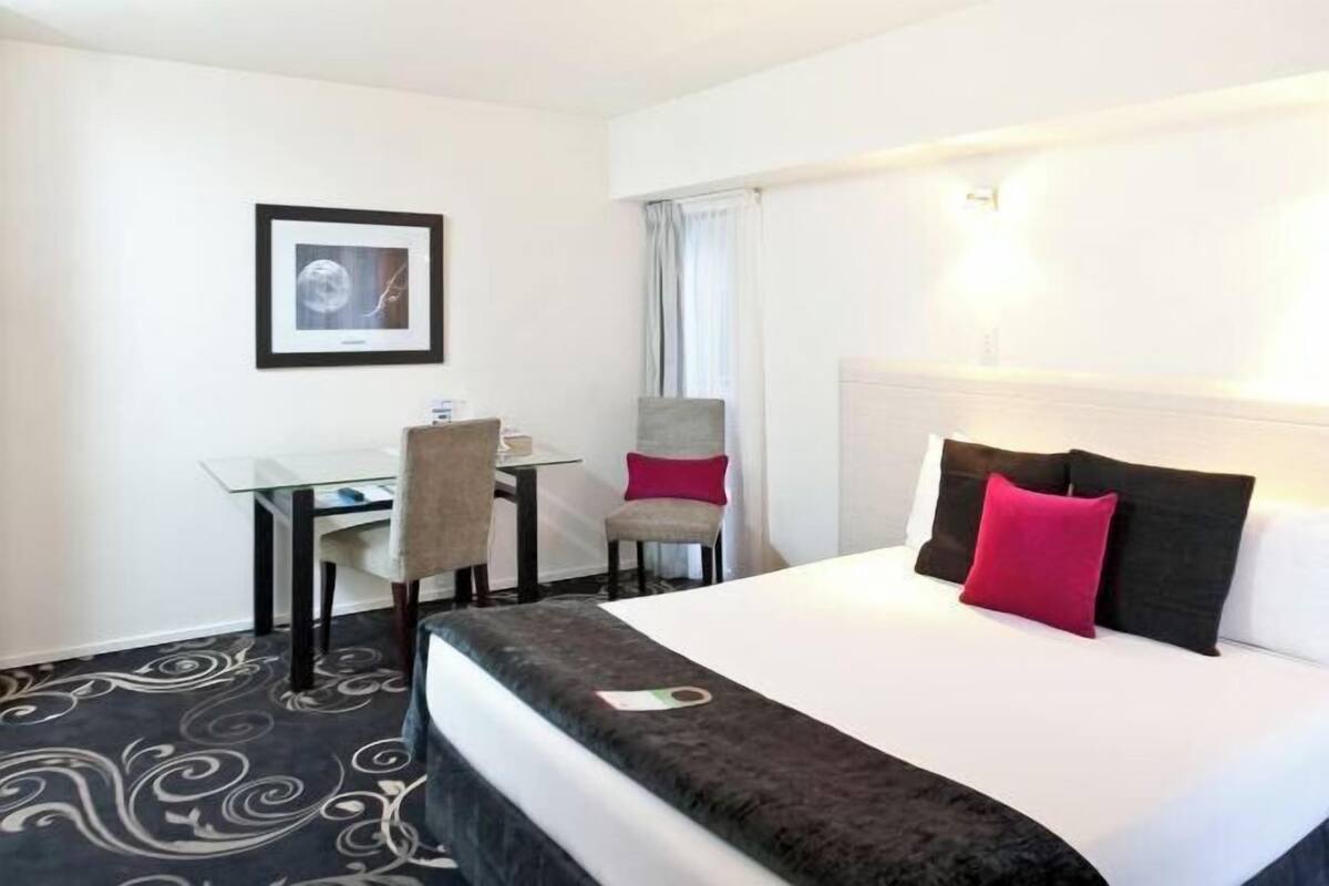 Ein Hotelzimmer mit einem Bett, einem Schreibtisch, einem Sessel und einem gerahmten Bild an der Wand.