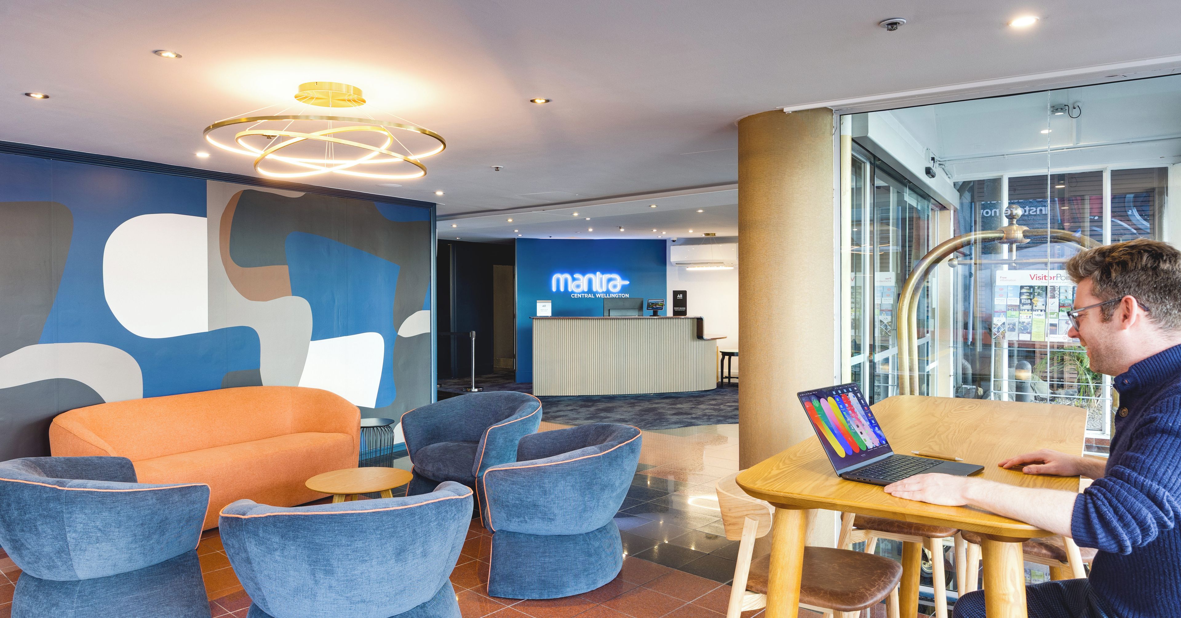 A modern hotel lobby with seating areas, a reception desk, and a view of the city through large windows.