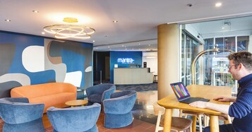 Una moderna hall dell'hotel con aree salotto, una reception e vista sulla città attraverso ampie finestre.