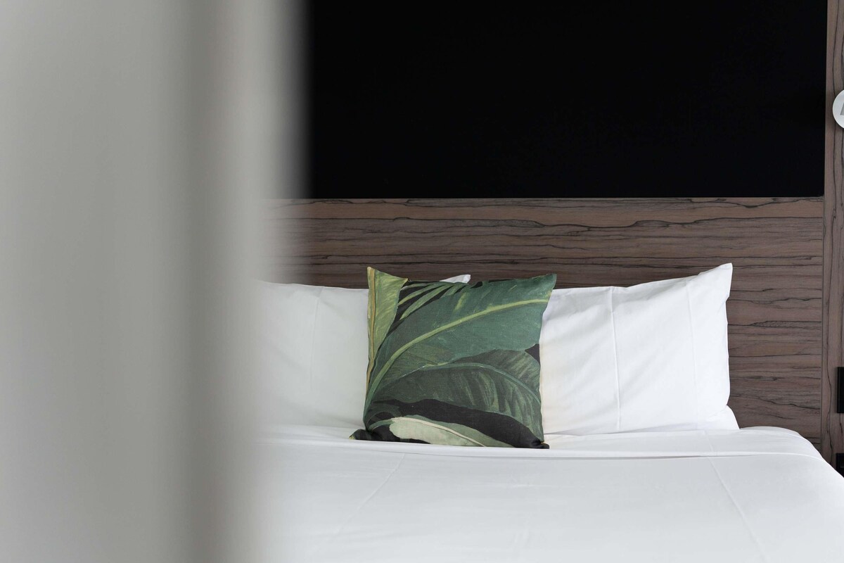 A bed with white bedding and a single green leaf-patterned pillow.