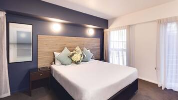 Une chambre d’hôtel avec un grand lit, une table de chevet, une tête de lit en bois et une grande fenêtre avec des rideaux.