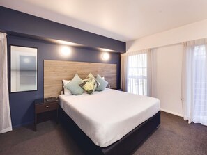 A hotel room with a large bed, a nightstand, a wooden headboard, and a large window with curtains. - Mantra Central Wellington  (Wellington)