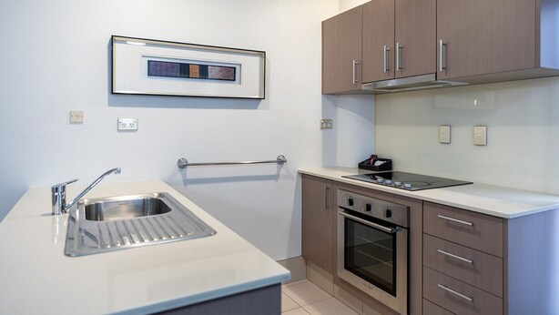 A compact kitchen with a sink, stove, oven, and a framed artwork above the counter.
