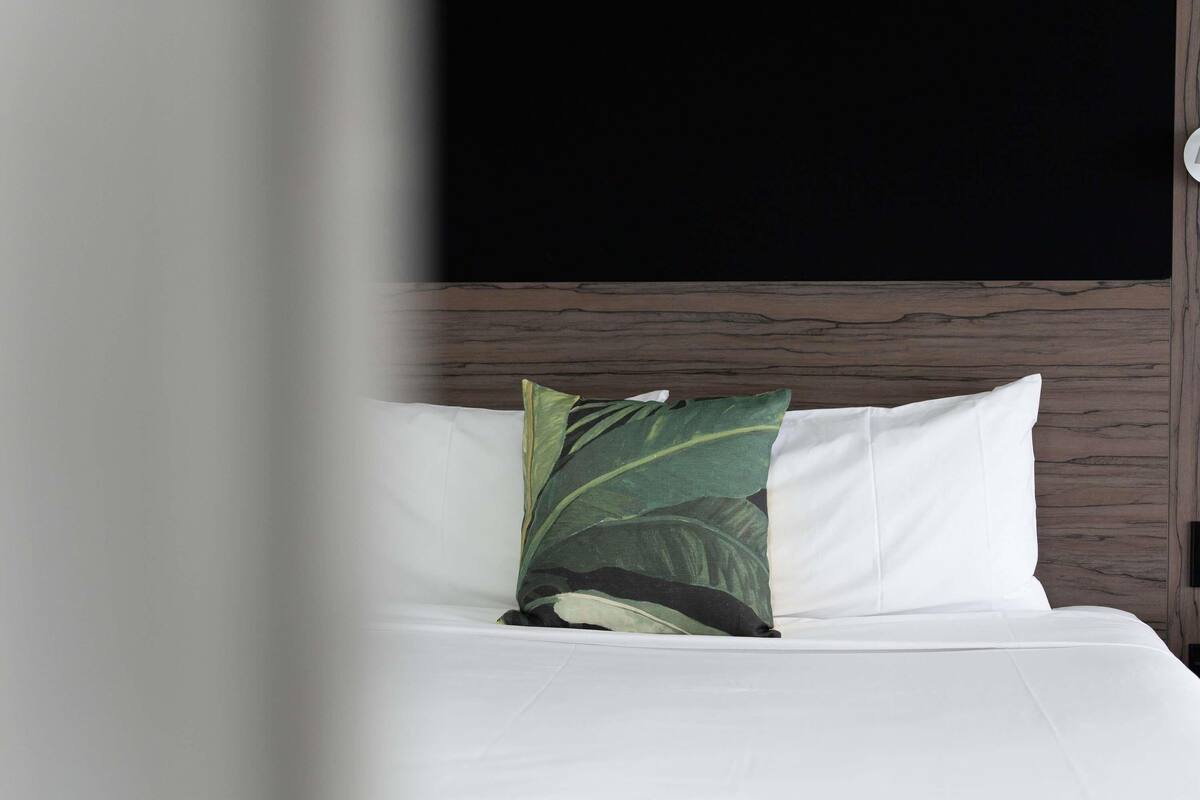Ein Bett mit weißer Bettwäsche und einem Kissen mit grünem Blattmuster.