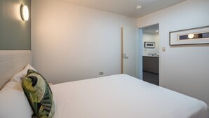 A hotel room with a bed, a pillow, a wall-mounted light, a door leading to a bathroom, and a framed picture on the wall.