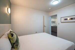Una camera d'albergo con un letto, un cuscino, una lampada a parete, una porta che conduce al bagno e un quadro appeso al muro.