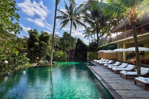 A poolside area with lounge chairs and umbrellas, surrounded by palm trees and a clear blue sky.