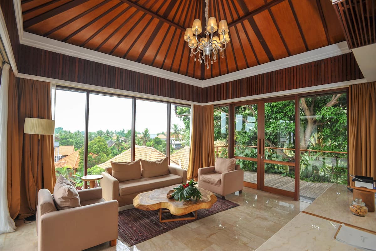 A spacious living room with a large window, a chandelier, and a wooden ceiling.