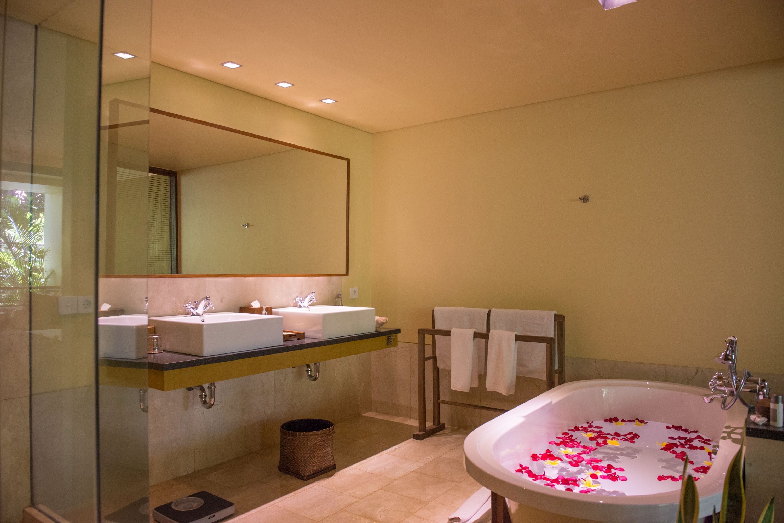 Ein modernes Badezimmer mit zwei Waschbecken, einer großzügigen Badewanne mit Rosenblüten und einer Duschkabine aus Glas.