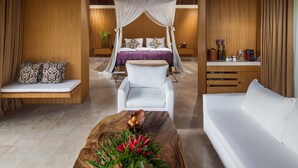 A bedroom with a canopy bed, a white sofa, a wooden coffee table, and a bedside table with decorative items. - Komaneka at Rasa Sayang (Ubud)