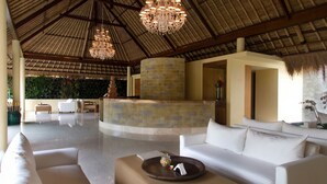 A spacious lobby with a high ceiling, a central seating area with white sofas, a stone reception desk, and a decorative chandelier. - Komaneka at Rasa Sayang (Ubud)