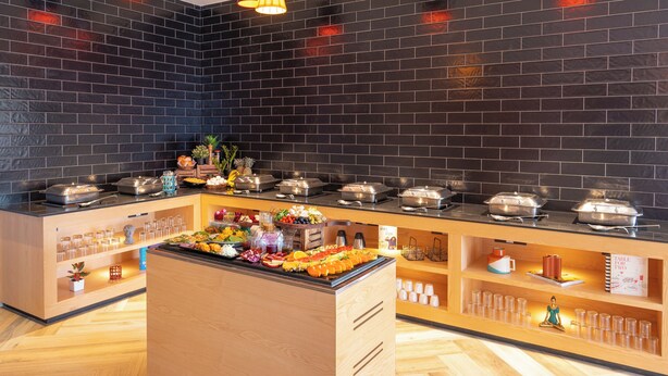 A buffet setup with various food items and drinks, a wooden counter, and a black-tiled wall. - Ginger Mumbai Andheri (MIDC) (Mumbai)