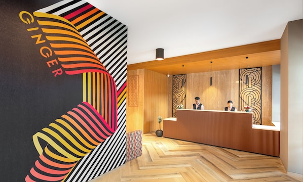 A reception area with a modern design, featuring a wooden reception desk, a large abstract wall art piece, and a herringbone patterned floor.