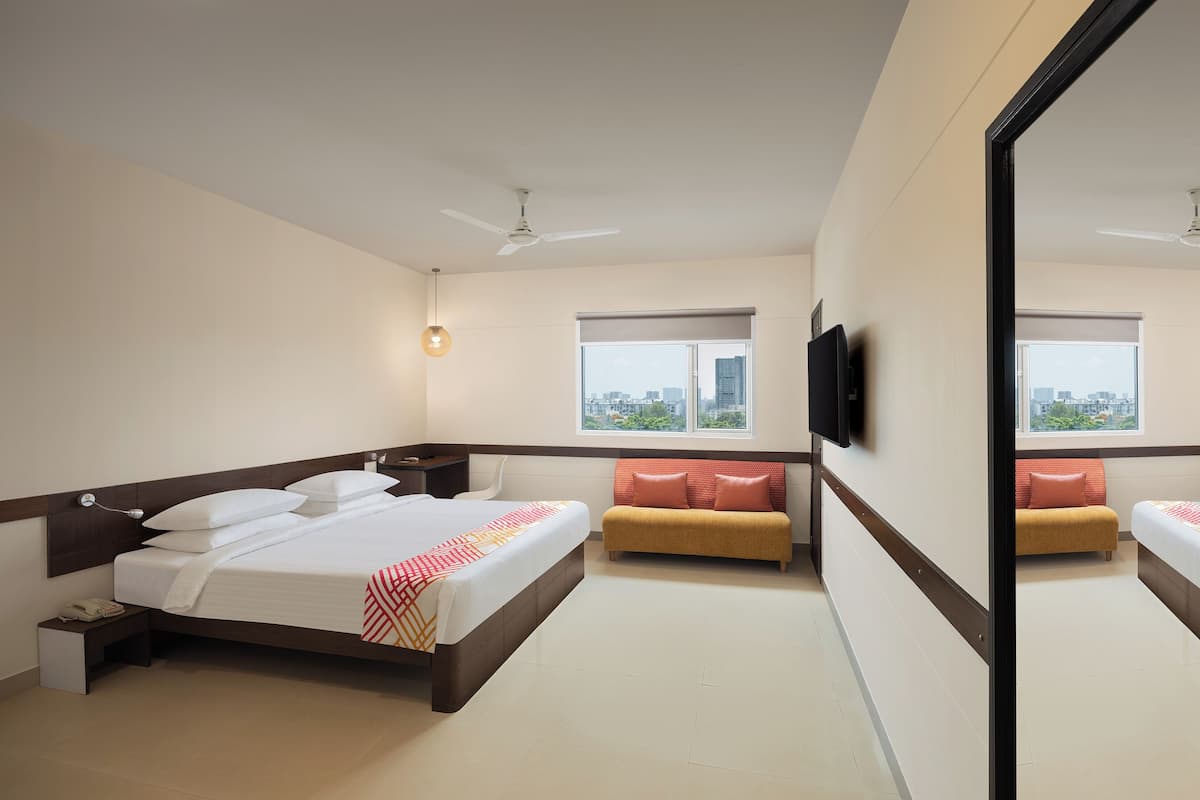Ein Hotelzimmer mit einem großen Bett, einer Couch, einem Fernseher und einem Fenster mit Blick auf die Stadt.