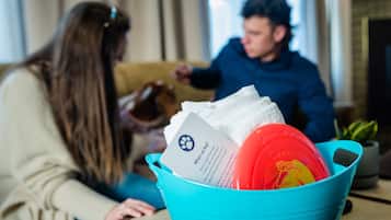 A person sitting on a couch with a dog, a blue bucket with a red bowl and a card.