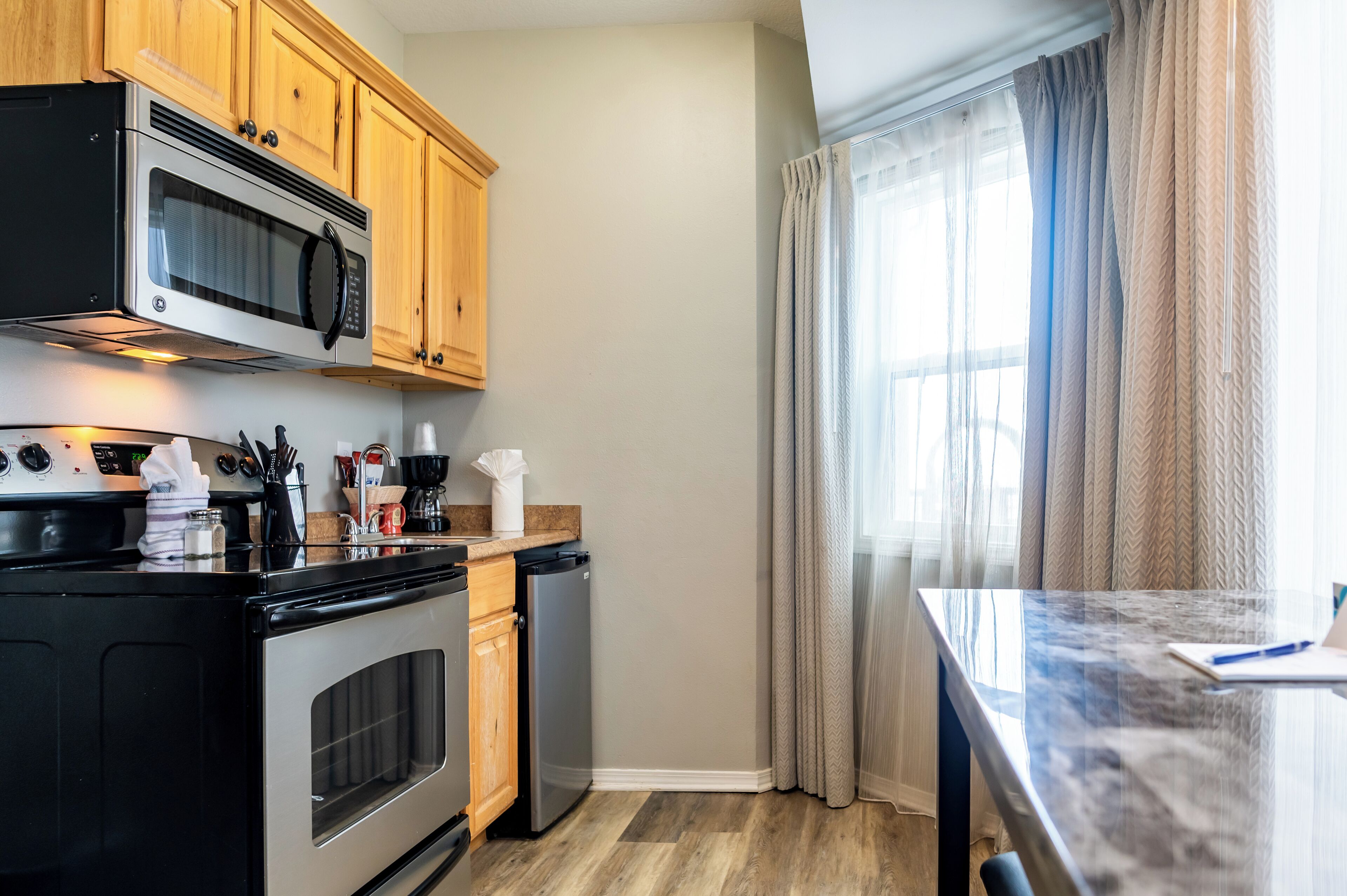 A compact kitchen with wooden cabinets, a stainless steel microwave, a built-in oven, and a dishwasher.