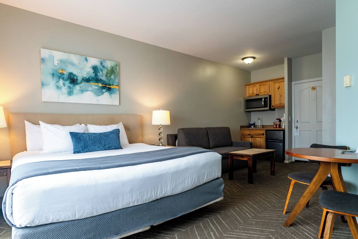 Ein Hotelzimmer mit einem großen Bett, einem Schreibtisch, einem Sessel, einer Mikrowelle und einer Küchenzeile.