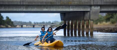 Two people kayaking on a river under a bridge.