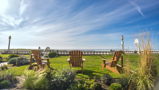 A grassy area with three wooden chairs facing a pier. - Inn at the Prom Oceanfront Seaside (Seaside)