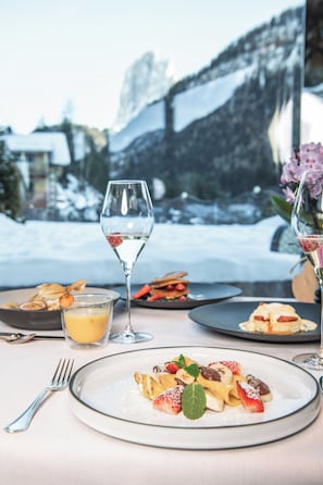 A dining table with plates of food, glasses of water, and a view of a snowy landscape. - ALPIN GARDEN LUXURY MAISON & SPA (Ortisei)