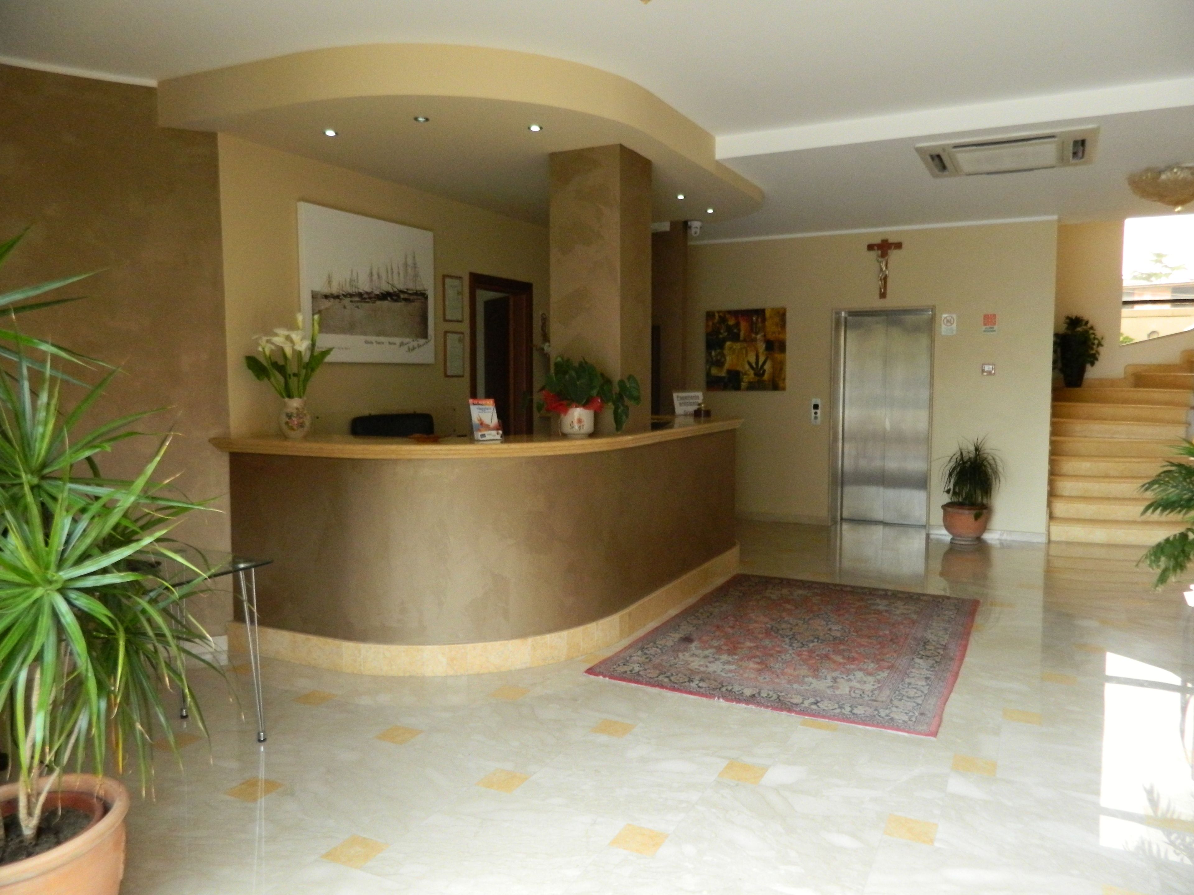 A reception area with a curved counter, potted plants, a framed picture, and a patterned rug.