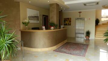 A reception area with a curved counter, potted plants, a framed picture, and a patterned rug.