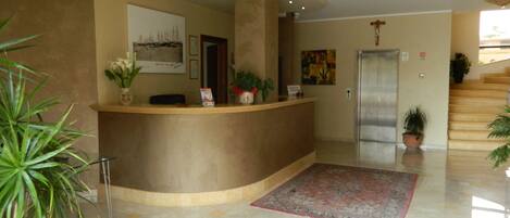 A reception area with a curved counter, potted plants, a framed picture, and a patterned rug.