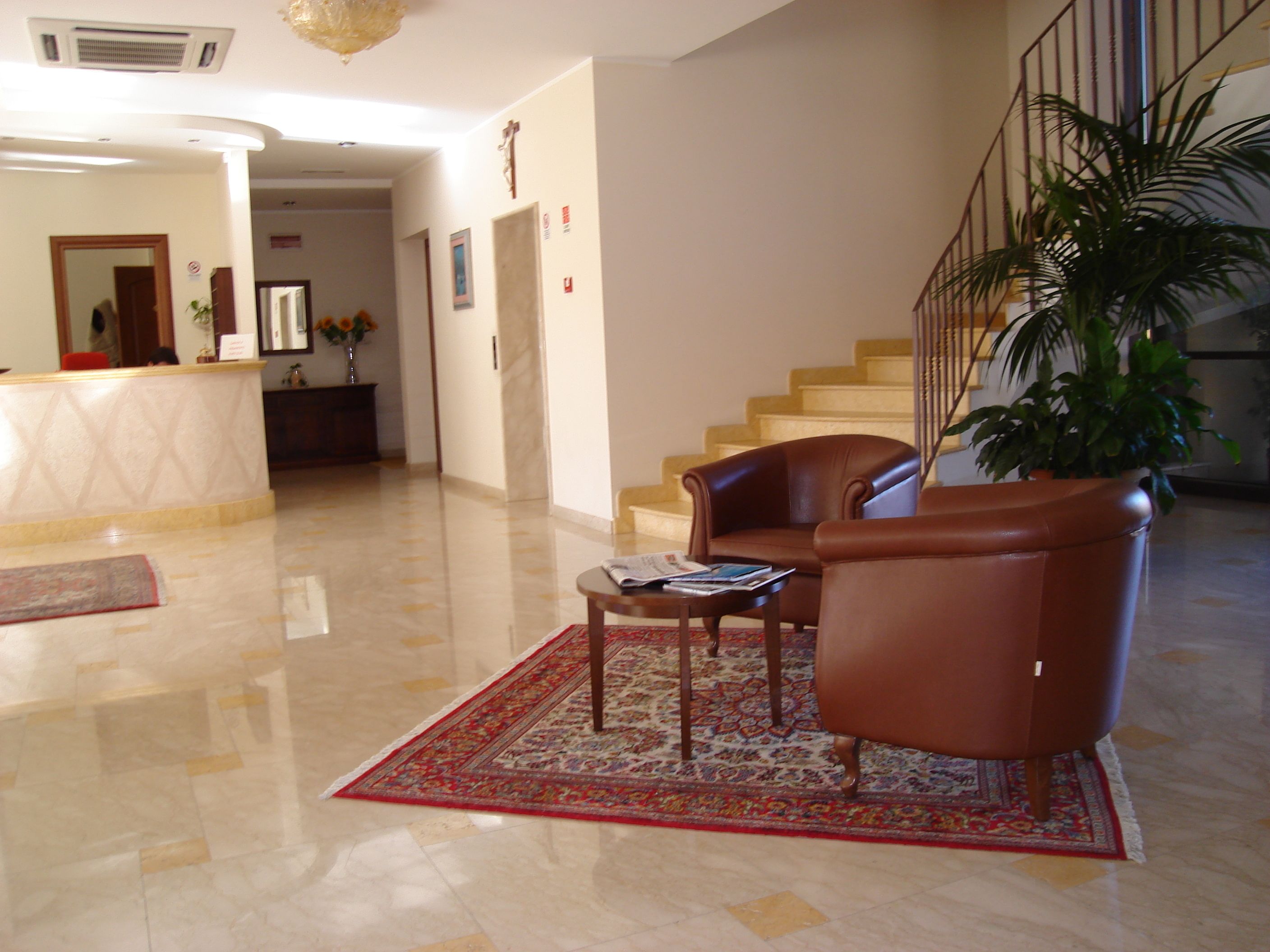 Un vestíbulo con mostrador de recepción, escalera, sillones de cuero, una mesa de centro y una planta grande en maceta.