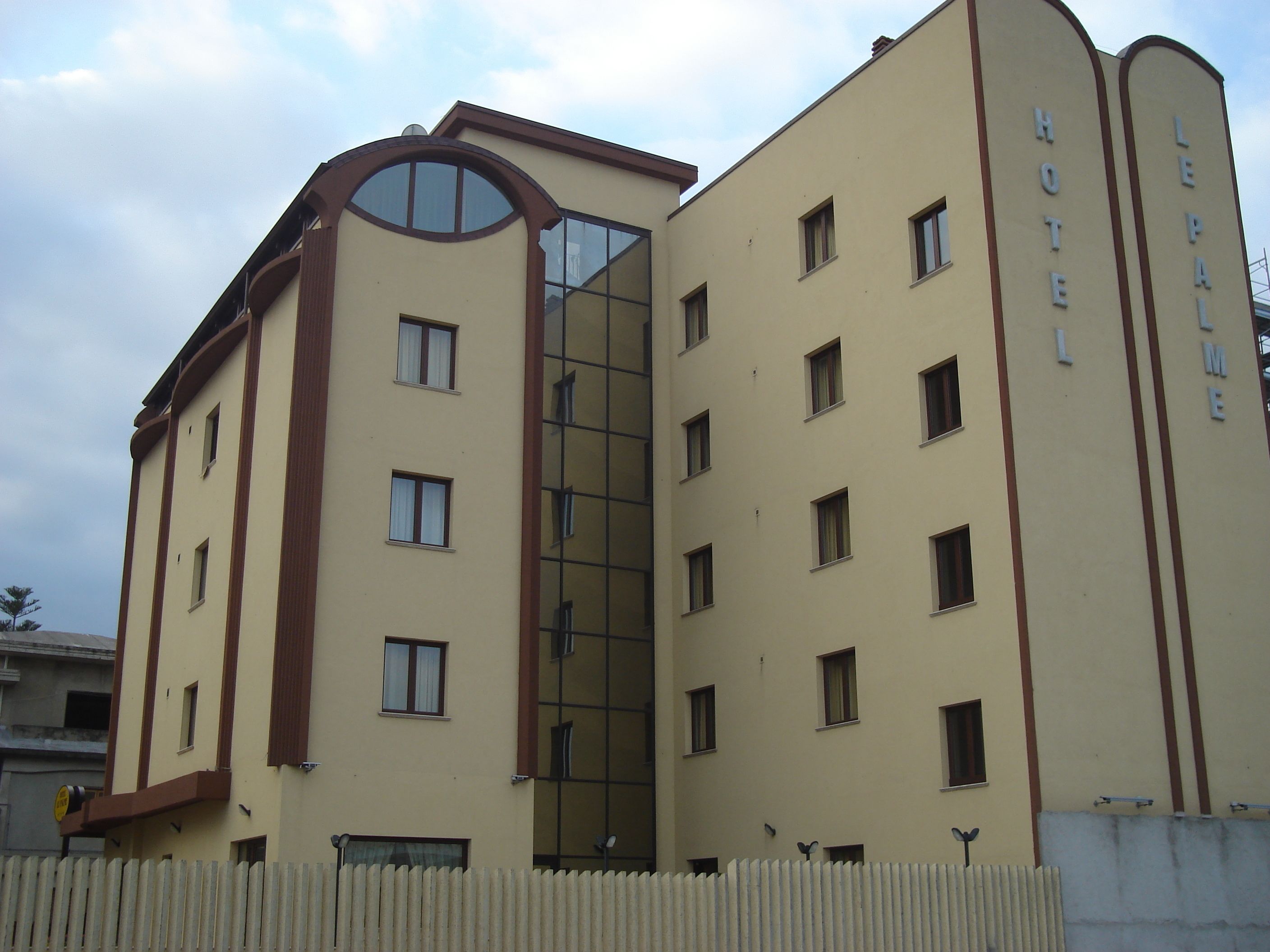 A hotel with a modern design, featuring a central glass elevator shaft, multiple windows, and a beige facade.