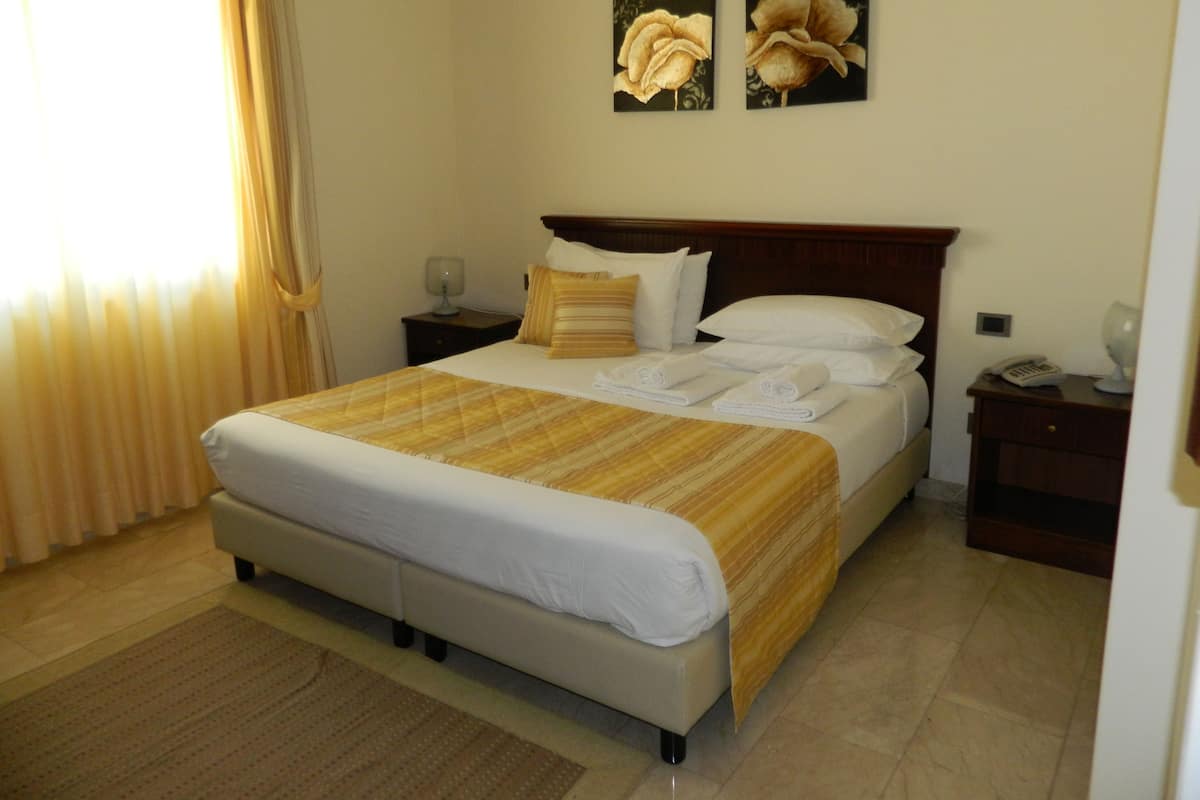 Une chambre d’hôtel avec un grand lit, deux tables de chevet, une petite table, une lampe et un téléphone.