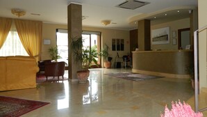 A spacious lobby with a reception desk, a large sofa, and several potted plants. - Hotel Le Palme (Gioia Tauro)