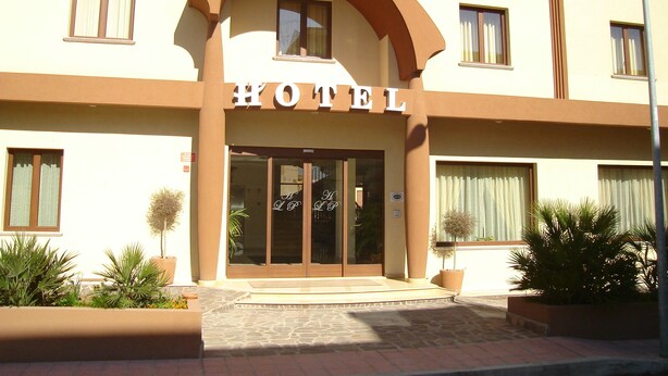 A hotel entrance with a large arched doorway, multiple windows, and potted plants. - Hotel Le Palme (Gioia Tauro)