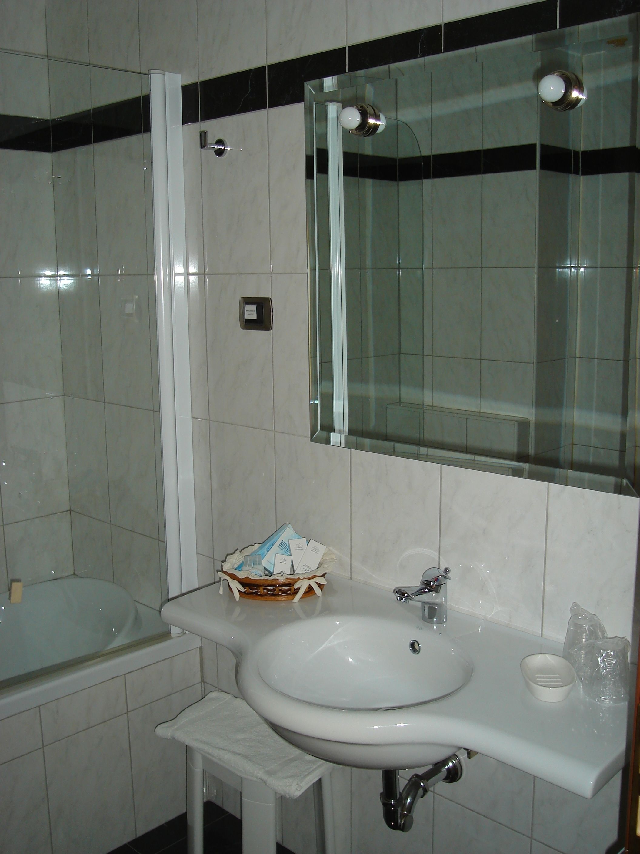 A bathroom with a white sink, mirror, and bathtub. There is a small basket with toiletries on the sink counter.