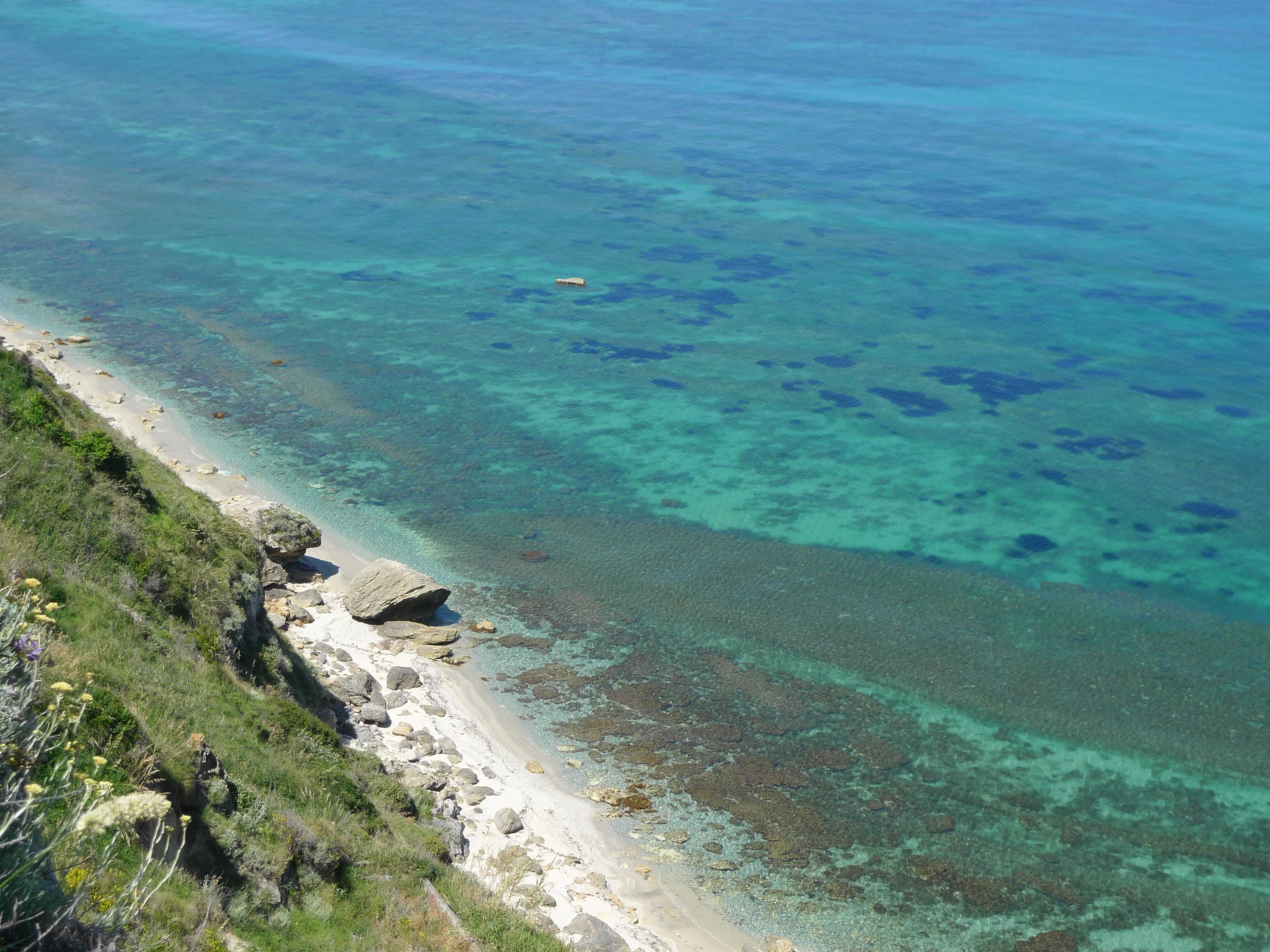 Una playa costera con aguas cristalinas, costa rocosa y vegetación.
